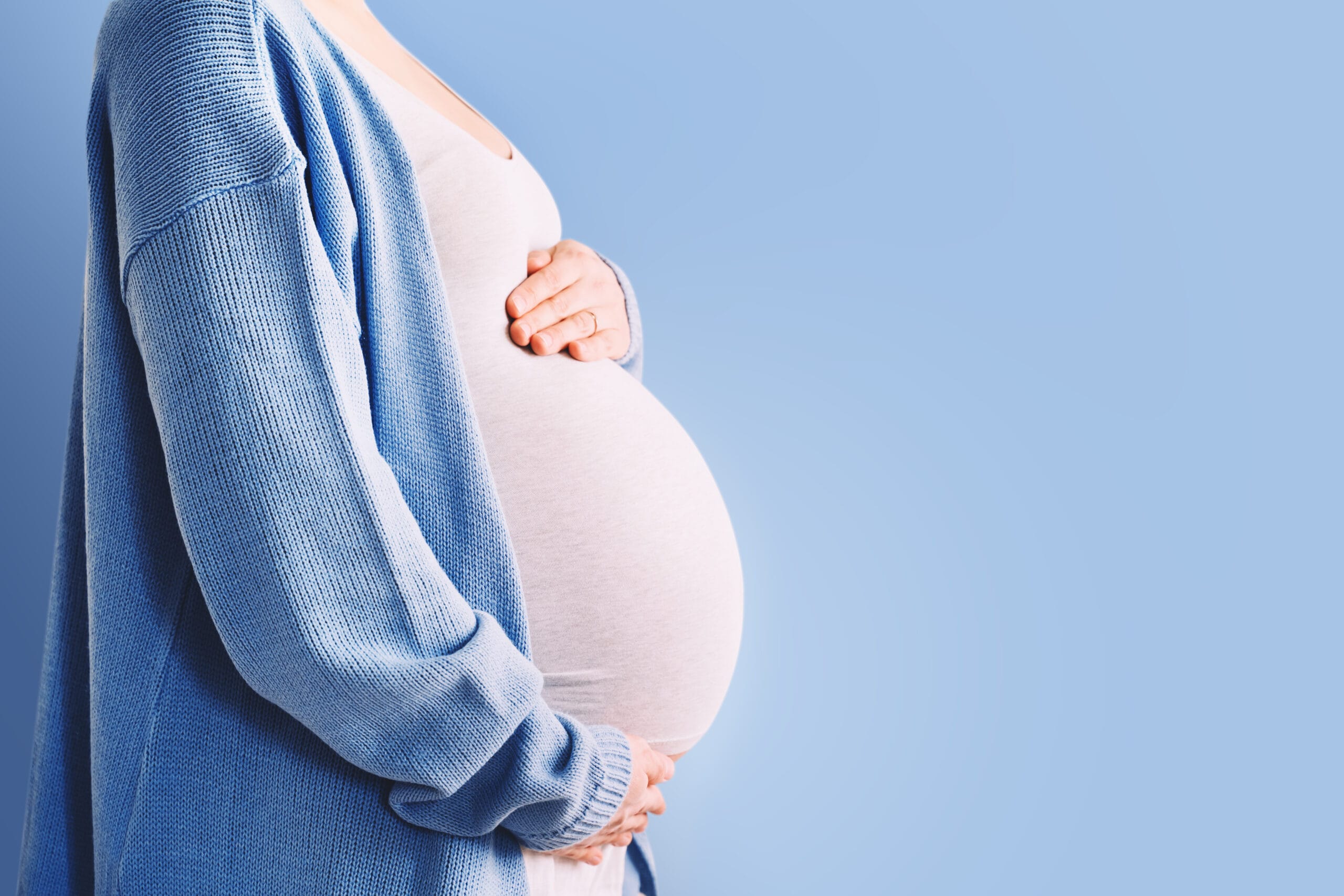 Beautiful pregnant woman hugging her belly in white background. Expectant mother waiting for baby birth during pregnancy. Concept of maternal health, visiting doctor and gynecological checkup. Royauté Medicina
